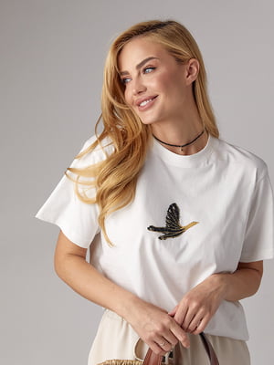 Трикотажна футболка молочного кольору прикрашена птахом зі страз | 6851483